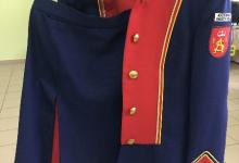 Zdjęcie przedstawia czerwono granatowy mundur wiszący na wieszaku, w składzie którego jest: żakiet i spódnica. 
