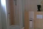 Zdjęcie przedstawia łazienkę, widać: kabinę prysznicową, toaletę. Łazienka wykończona jest różnej wielkości białymi i beżowymi  i brązowymi płytkami.