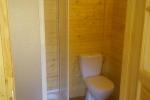 Zdjecie przedstawia wnętrze łazienki widać toaletę i prysznic. Łazienka wykończona jest drewnianymi panelami