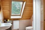 Zdjęcie przedstawia wnętrze łazienki na suficie drewniane panele, ściany wykończone białymi płytkami.  Na zdjęciu widać kabinę prysznicową, zlew, toaletę.