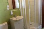 Zdjęcie przedstawia łazienkę, widać: toaletę, zlew z białą szafką oraz kabinę prysznicową. Nad zlewem znajduje się lustro oraz lampa ścienna. Łazienka wykończona jest zielonymi płytkami.