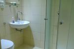 Zdjęcie przedstawia łazienkę widać: białą toaletę, zlew, kabinę prysznicową, lustro. Łazienka wykończona jest białymi płytkami
