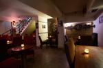 Szuflada Cafe&Bar Zdjęcie przedstawia wnętrze restauracji Szuflada Cafe&Bar. Na ścianach widoczne ozdoby oraz obrazy i zdjęcia. W ponieszczniu widać duży podłużny drewniany stół, oraz kilka małych okrągłych stolików. Obok stołu i stolików stoją Krzesła obite bordowym materiałem.