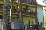 Zdjęcie przedstawia budynek hotelu Wojciech z zewnątrz. Na tarasie widoczne szare okrągłe stoliki z szarymi krzesłami Na zdjęciu przed budynkiem widoczne drzewa