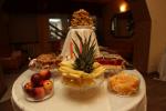 Zdjęcie przedstawia okrągły stolik zastawiony jedzeniem: salaterki z owocami, półmiski z ciastem. 