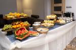 Zdjęcie przedstawia stół zastawiony jedzeniem, na którym znajdują się: tależe z owocami, ciasta. Na stole stoją tależę oraz filiżanki. 