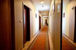 Zdjęcie przedstawia korytarz hotelowy w Centrum Młodości Villa & Fitness Club. Po lewej stronie widać drewniane drzwi pomiędzy którymi wiszą obrazy. Na zdjęciu widoczny wąski  brązowy dywan.